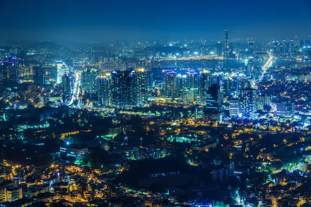 Aerial view of the illuminated skyscrapers and bustling cityscape of Seoul, South Korea, at night. The HD image captures the vibrant lights and buildings, making it a stunning desktop wallpaper and background.