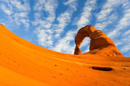 Fisheye view of Delicate Arch under a partly cloudy sky in Arches National Park, Utah, USA, showcasing striking natural rock formations and vibrant orange sandstone.