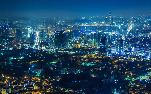 Aerial view of the illuminated skyscrapers and bustling cityscape of Seoul, South Korea, at night. The HD image captures the vibrant lights and buildings, making it a stunning desktop wallpaper and background.