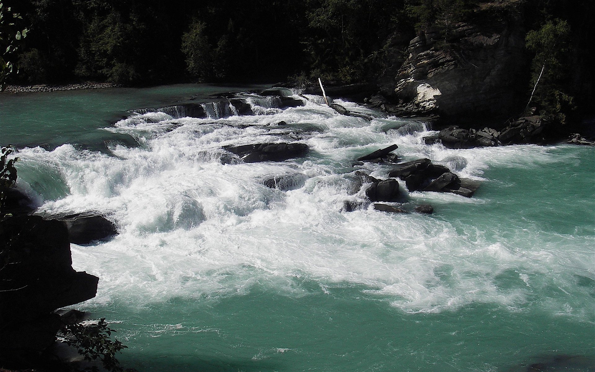 HD PC desktop wallpaper background: nature scene of a turquoise river tumbling over rocks into white rapids beneath forested banks.