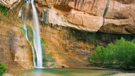HD desktop wallpaper featuring Calf Creek Falls cascading down a rocky cliff into a serene pool, surrounded by lush greenery and natural rock formations.