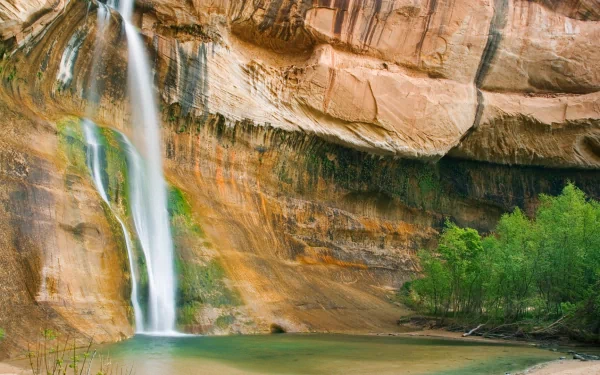 HD desktop wallpaper featuring Calf Creek Falls cascading down a rocky cliff into a serene pool, surrounded by lush greenery and natural rock formations.