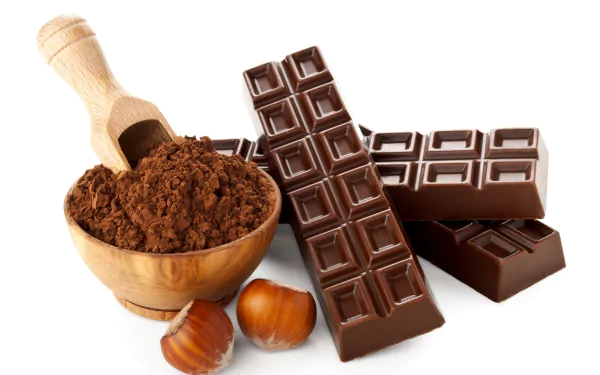 Close-up of chocolate bars, cocoa powder in a wooden bowl with a scoop, and hazelnuts, captured in 8K Ultra HD for a vibrant PC desktop wallpaper background.
