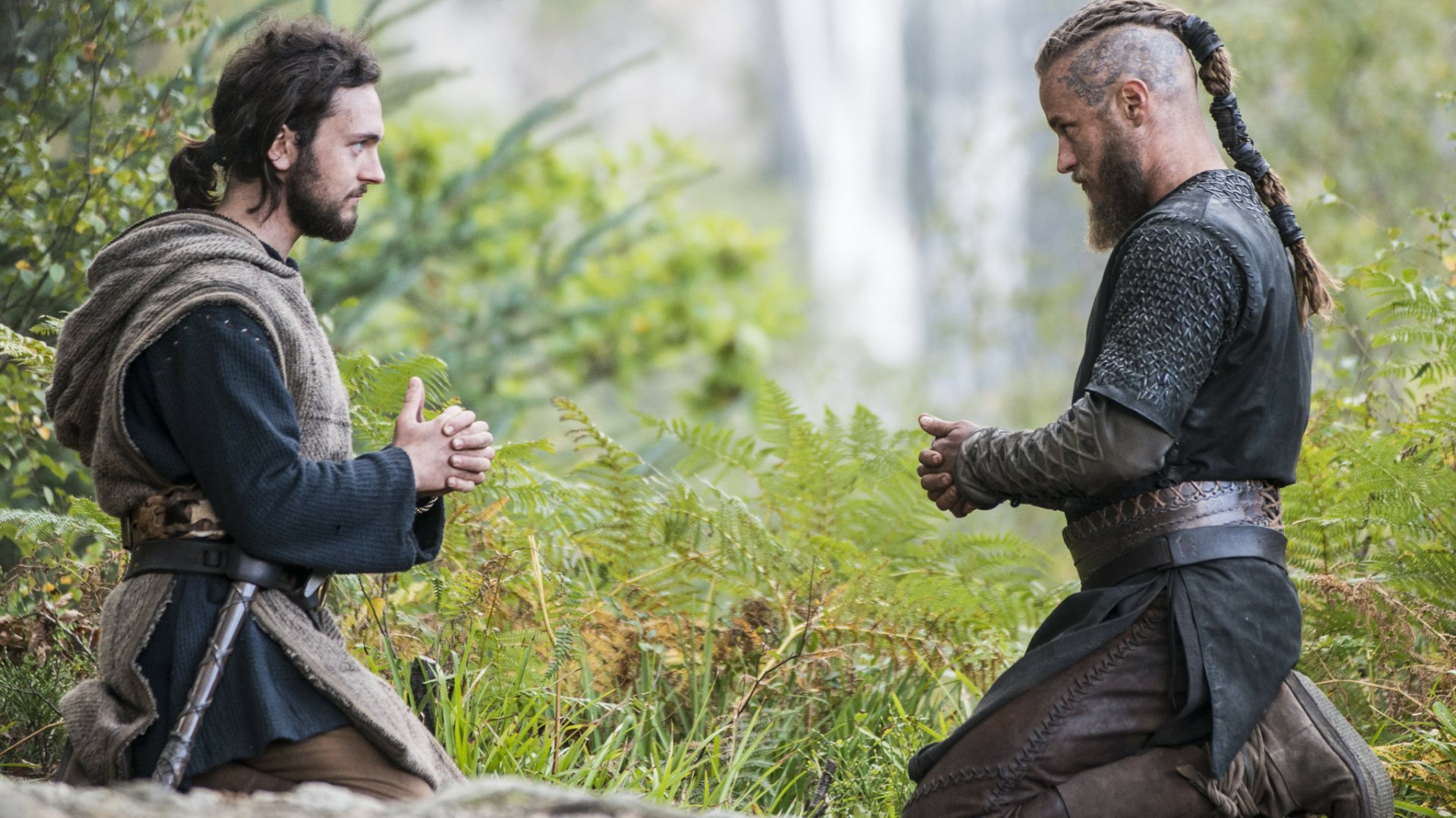 HD desktop wallpaper featuring two characters from the TV show Vikings (2013) kneeling and conversing in a lush green outdoor setting.