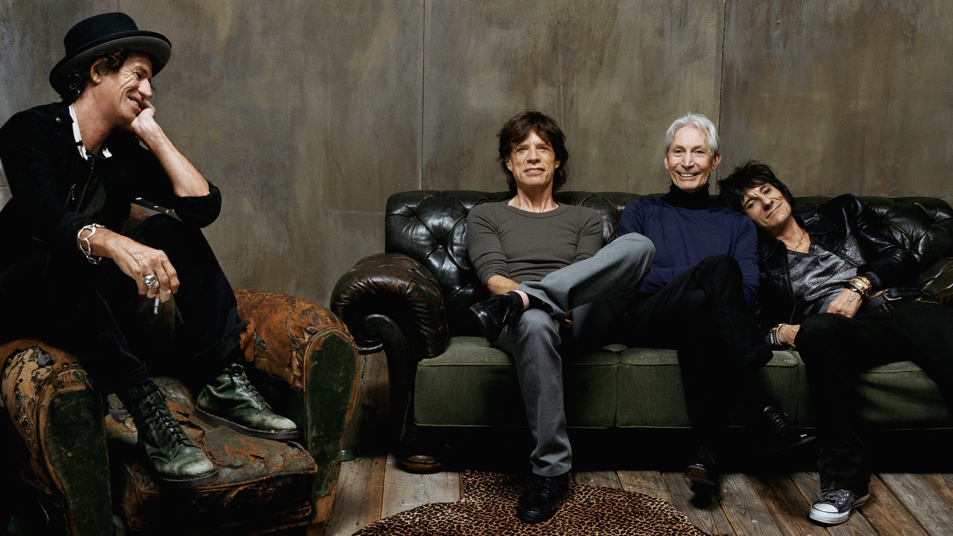 The Rolling Stones band members relaxed on vintage leather sofas, captured in an HD music-themed PC desktop wallpaper and background.