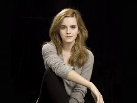 HD desktop wallpaper featuring celebrity Emma Watson seated against a black background, wearing a gray sweater, and looking at the camera with a serene expression.