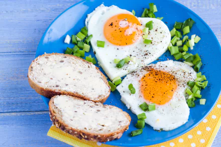 5K Ultra HD PC desktop wallpaper: heart-shaped fried eggs with bright yolks on a blue plate, chopped green onions and sliced buttered multigrain bread.