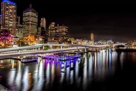 Night view of Brisbane city skyline and freeway along the Brisbane River with illuminated wharf and building reflections in Queensland, Australia.