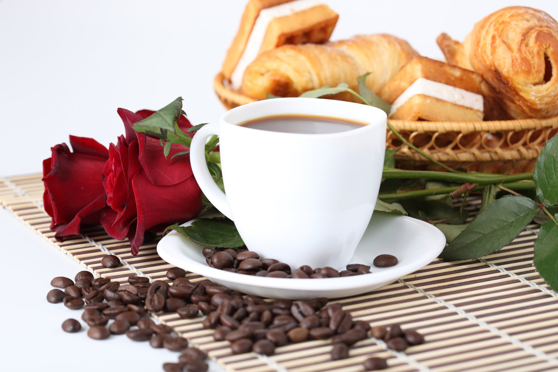 8K Ultra HD PC desktop wallpaper: still life of a white coffee cup on a saucer with scattered coffee beans, red roses and a basket of croissants.