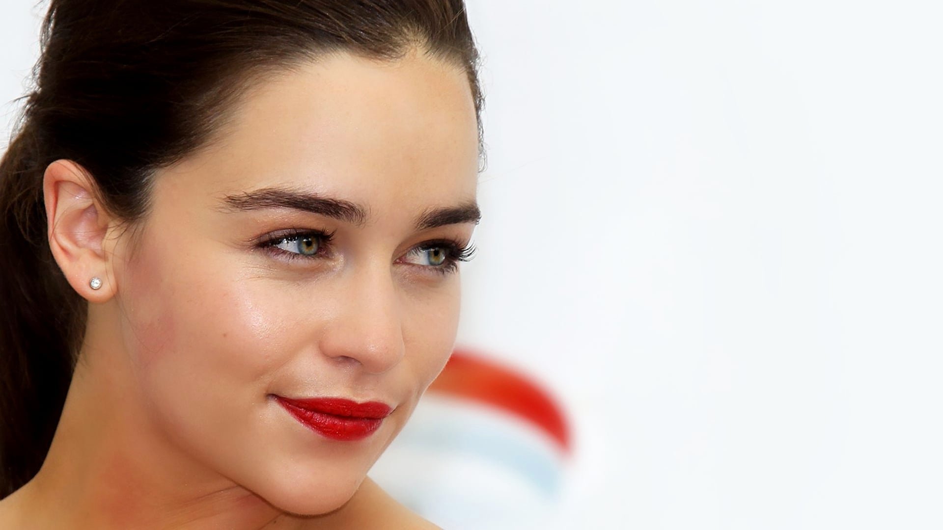 Close-up HD wallpaper of actress Emilia Clarke with striking blue eyes, red lipstick, and a soft smile, showcasing her English celebrity charm.
