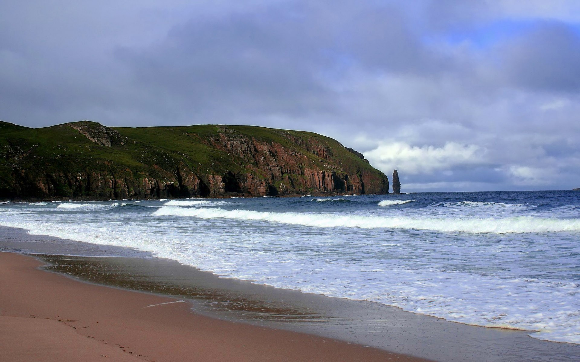 Coastal landscape with sandy beach, cliff, and tide along the shoreline.