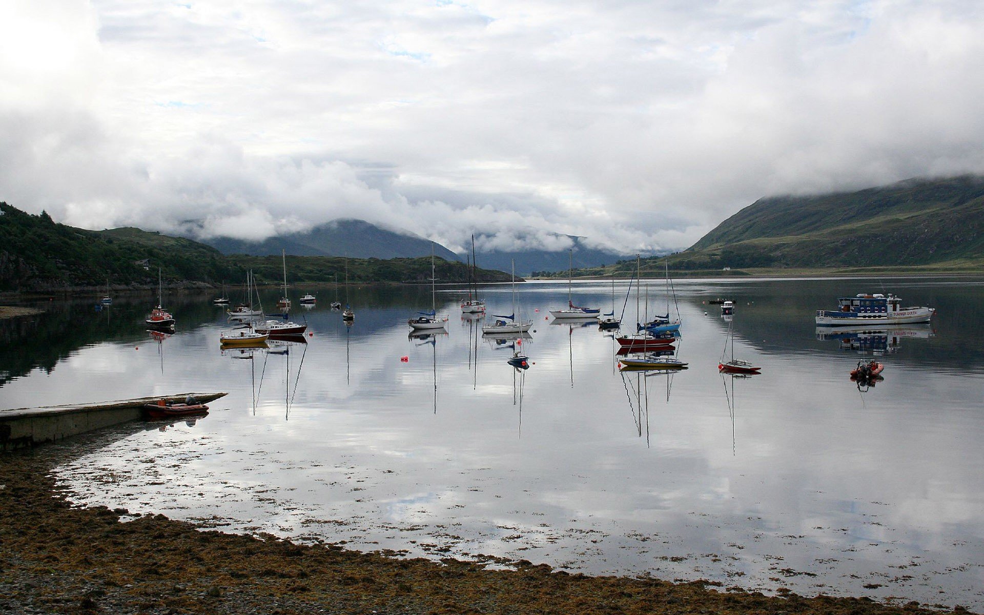 A serene fjord harbor with sailboats and ships docked at low tide, surrounded by misty hills and calm bay waters, captured in an HD landscape photography wallpaper.