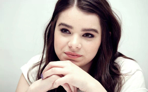 Close-up HD portrait of American actress Hailee Steinfeld with brunette hair and brown eyes, set against a plain light background.