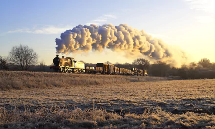 HD desktop wallpaper of a steam train locomotive emitting plumes of smoke as it travels through a frosty, open landscape with a clear sky in the background.