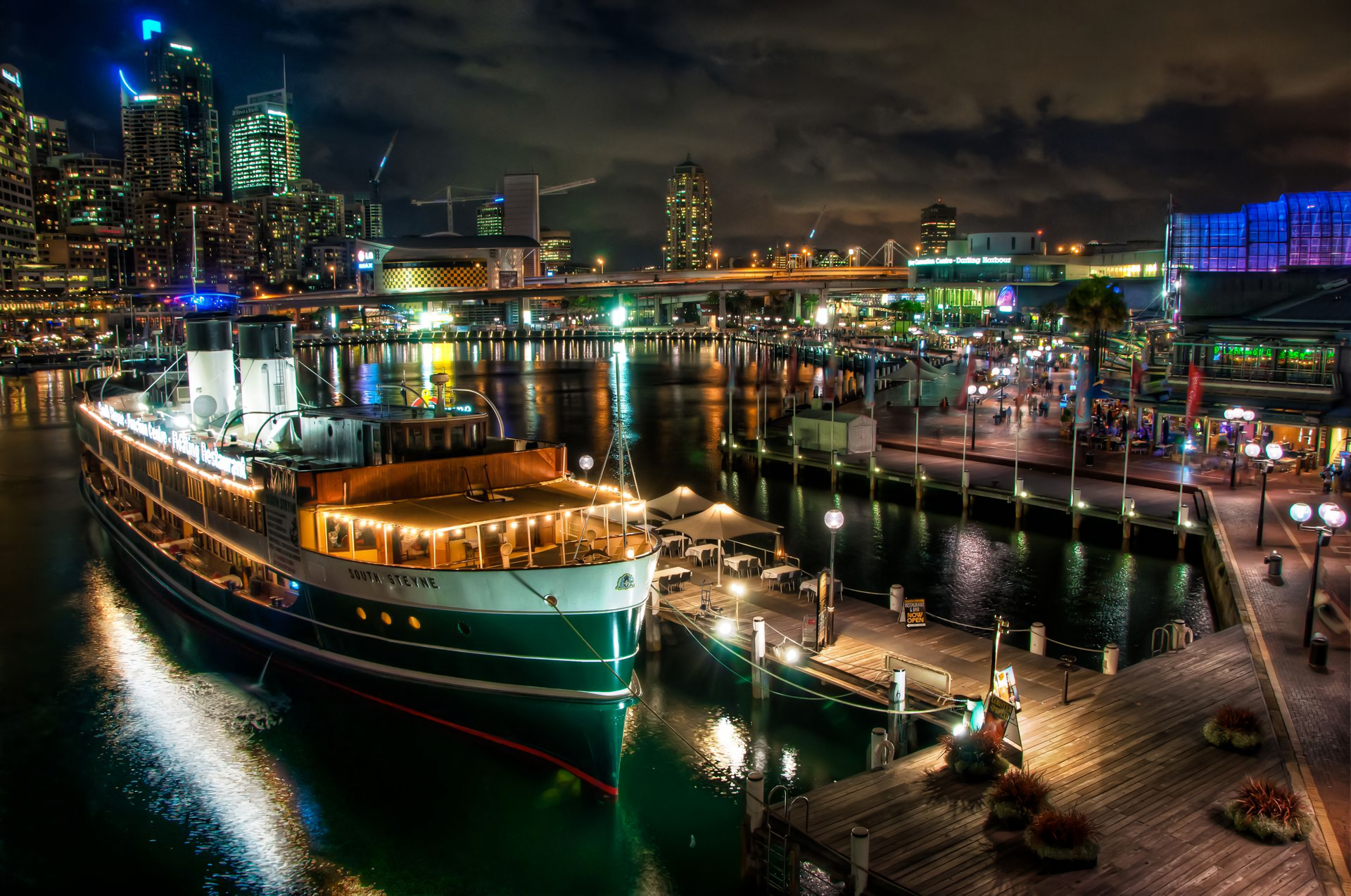 Night view of Sydney's Darling Harbour marina featuring the illuminated South Steyne Floating Restaurant boat and city lights, captured in HD for a desktop wallpaper.