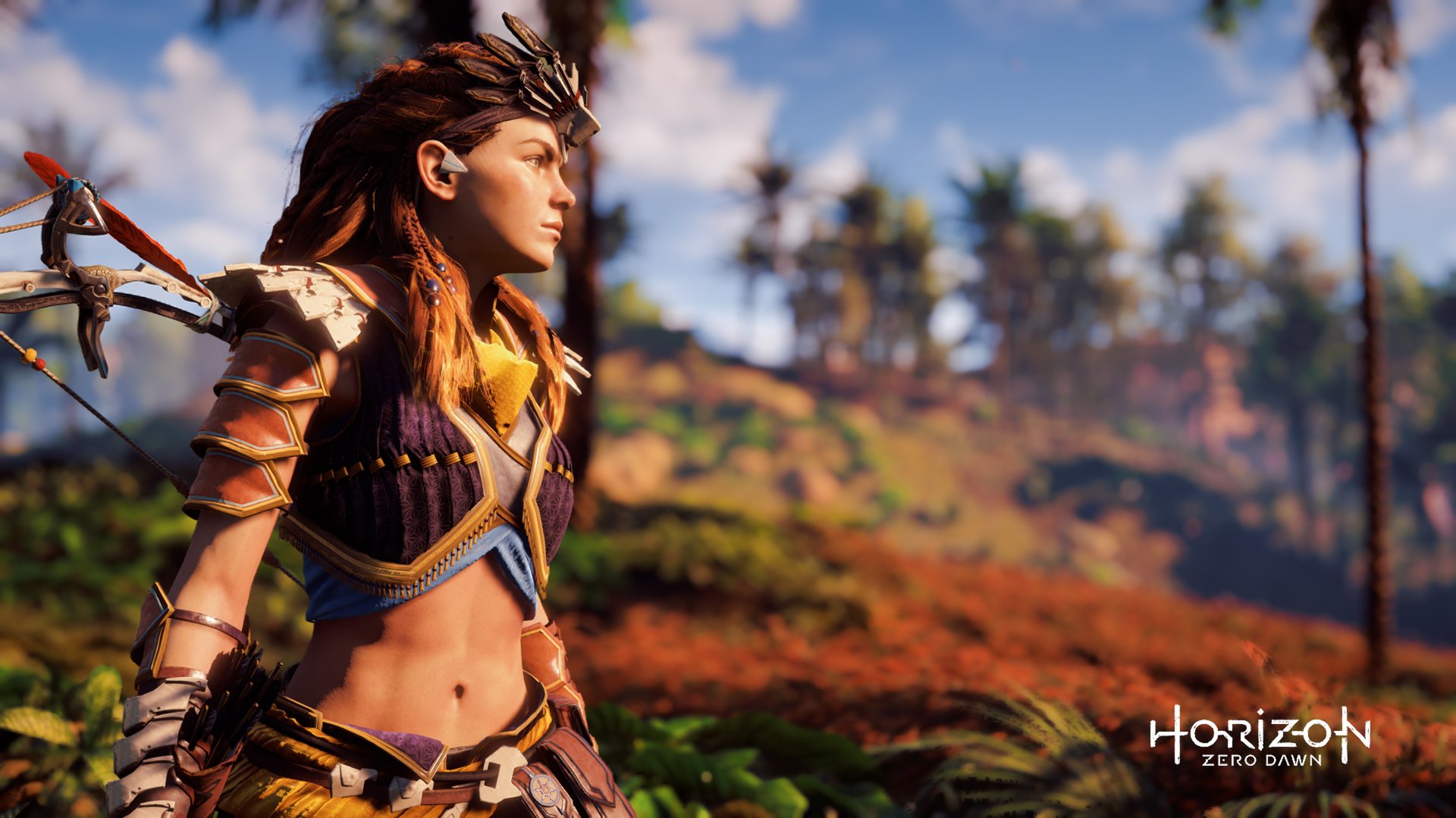 HD desktop wallpaper featuring Aloy from the video game Horizon Zero Dawn, standing in a vibrant, natural landscape with lush greenery and a clear blue sky.
