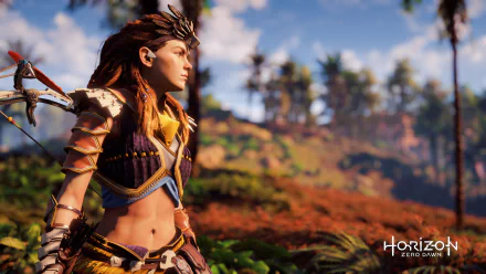 HD desktop wallpaper featuring Aloy from the video game Horizon Zero Dawn, standing in a vibrant, natural landscape with lush greenery and a clear blue sky.