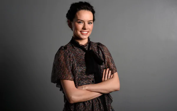 HD desktop wallpaper featuring brunette actress and celebrity Daisy Ridley smiling confidently against a plain gray background.