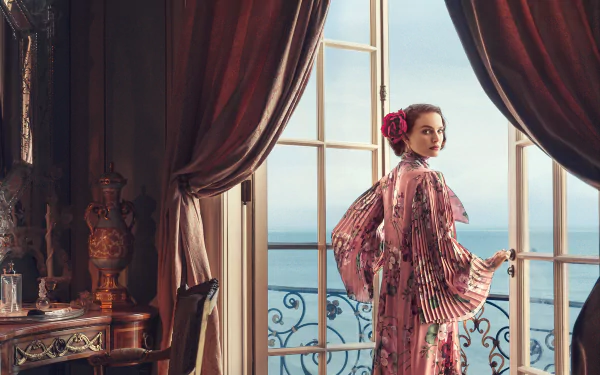 Actress Natalie Portman in a pink dress stands by a window overlooking the sea, creating an elegant HD desktop wallpaper with rich curtains and classic decor.