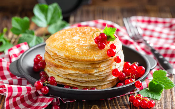 Still life of a stack of golden crêpes topped with red currants and green leaves on a skillet and red-checkered cloth — 5K Ultra HD PC wallpaper/background.