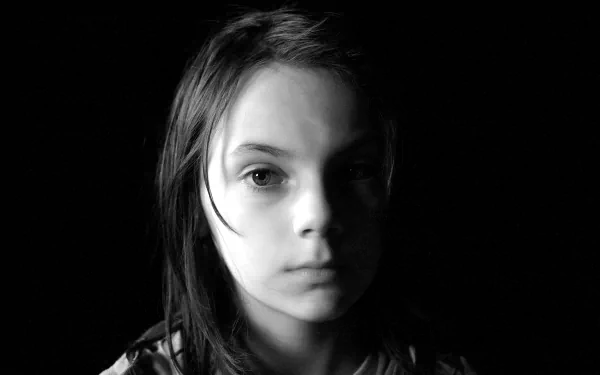 Black and white HD wallpaper featuring Dafne Keen as Laura Kinney (X-23) from the movie Logan. The image portrays a close-up shot with a dark background.