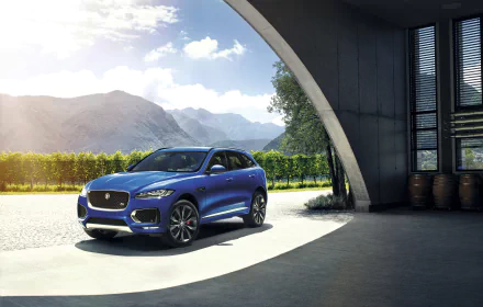 A blue Jaguar F-PACE SUV parked in a sunlit modern architectural setting with mountains and greenery in the background, shown in 4K Ultra HD quality.