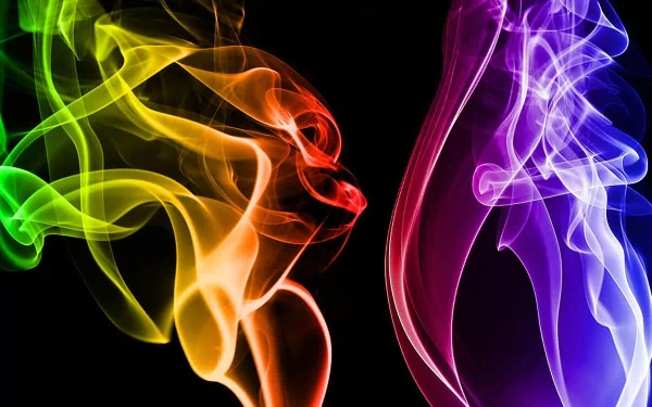 An abstract HD desktop wallpaper featuring vibrant smoke in shades of green, yellow, orange, and purple, swirling dynamically against a black background.