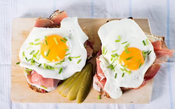 5K Ultra HD PC desktop wallpaper: food — two open-faced sandwiches topped with sunny-side-up eggs, prosciutto, chives and pickle slices on a wood board.