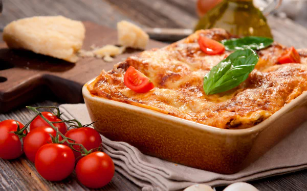 HD still life desktop wallpaper featuring a baked lasagna with melted cheese, fresh basil, cherry tomatoes, and rustic bread on a wooden table.