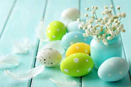 Colorful Easter eggs and white flowers in a jar on a light blue wooden surface, accompanied by delicate white feathers. HD desktop wallpaper and background for the Easter holiday.