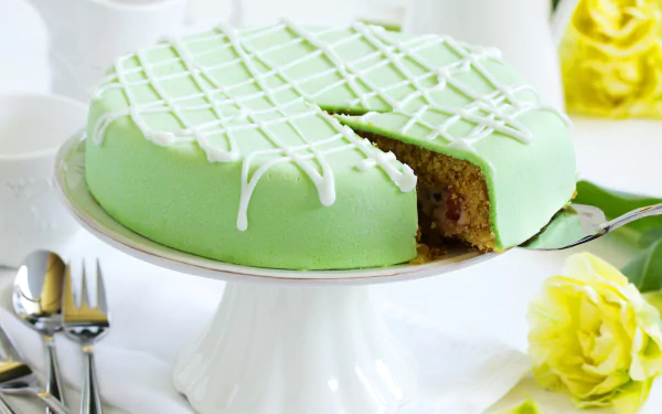4K Ultra HD PC desktop wallpaper: green-iced pastry cake on a white pedestal with a slice removed, food styling with utensils and yellow flowers on a bright table.