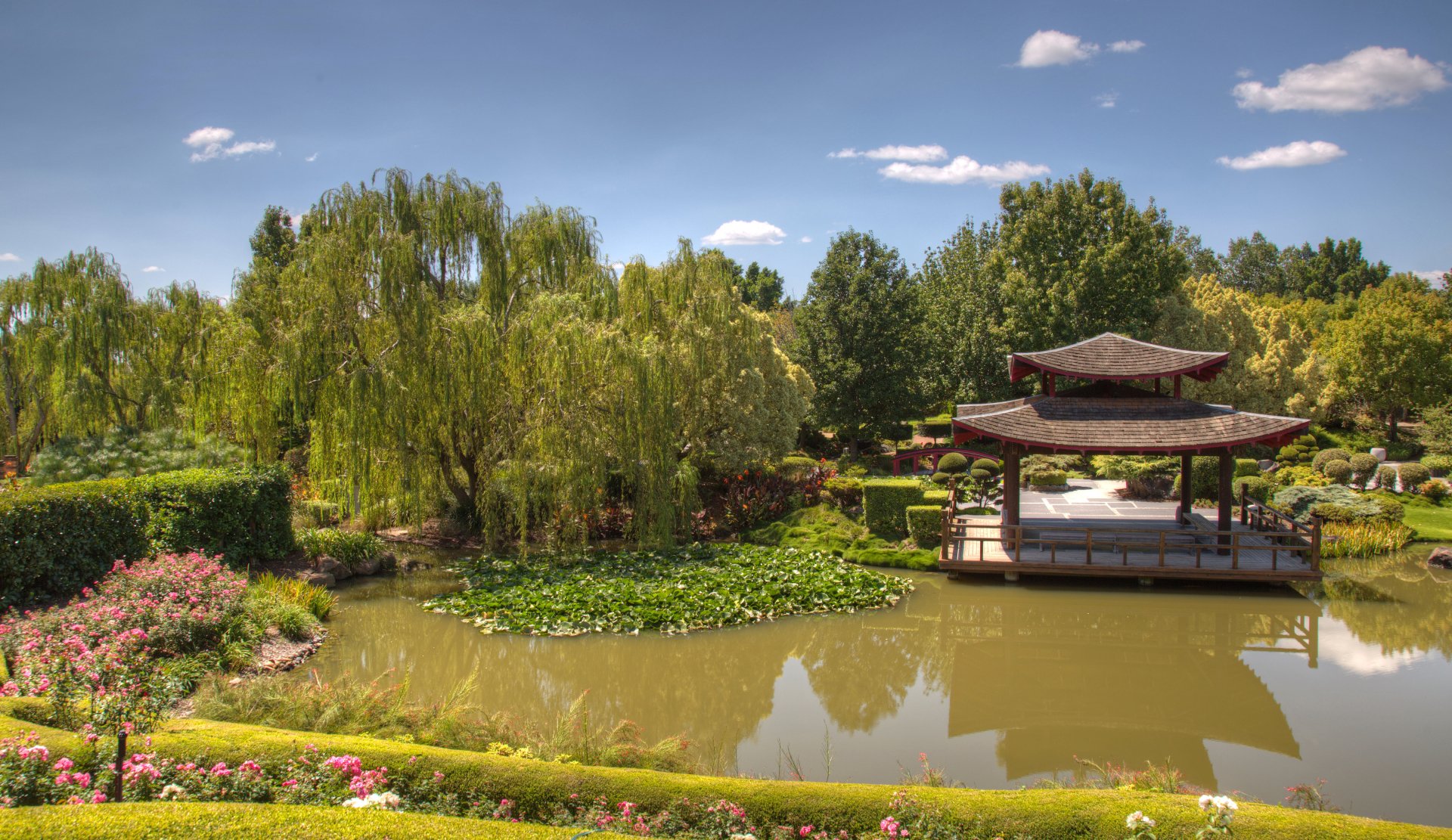 4K Ultra HD desktop wallpaper of a Japanese garden park: a tree-lined pond with lily pads, a wooden pagoda over the water and manicured flowerbeds.
