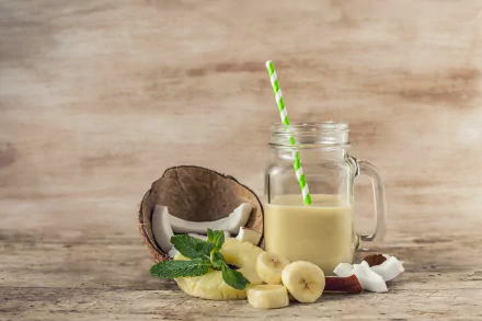4K Ultra HD wallpaper featuring a creamy coconut smoothie in a glass jar with a green-striped straw, sliced banana, coconut halves, and fresh mint on a rustic wooden surface.