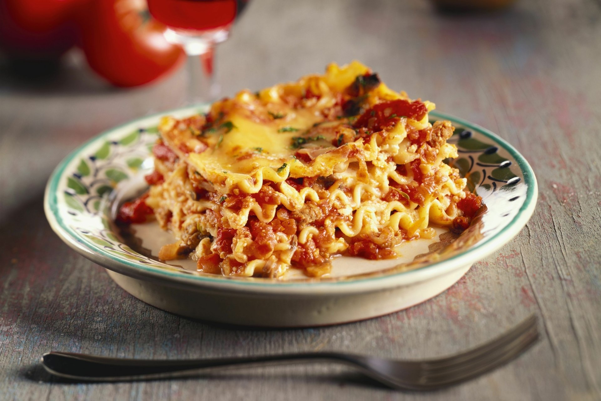 2K Quad HD PC desktop wallpaper: close-up meal of lasagna on a patterned plate, layered pasta, rich meat-tomato sauce and melted cheese with a fork nearby.