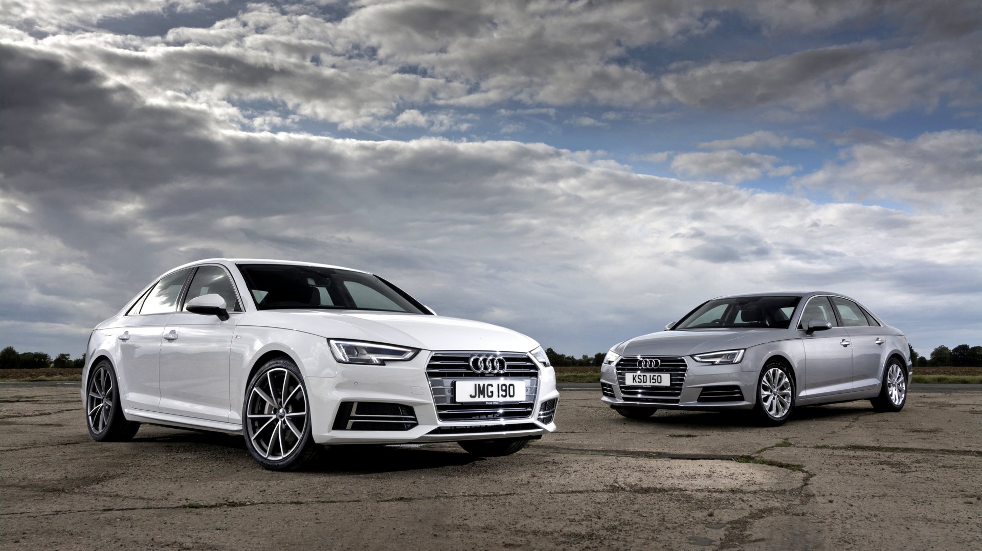 HD desktop wallpaper featuring two Audi A4 vehicles, one silver and one white, parked side by side under a dramatic cloudy sky.
