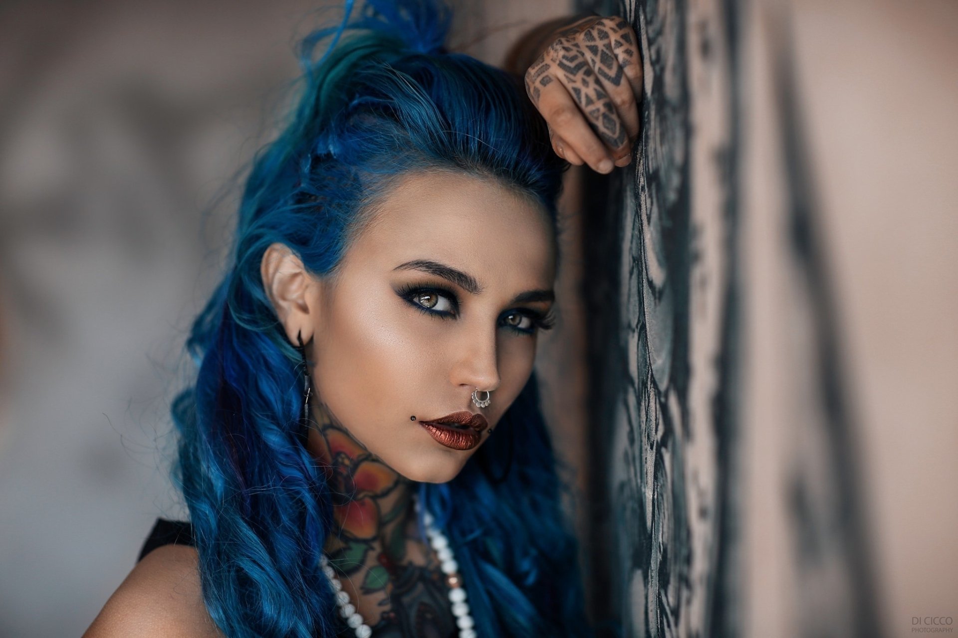HD desktop wallpaper of a tattooed woman with blue and hazel eyes, vibrant blue hair, and bold lipstick, posing close to an ornate wall, showcasing a striking model face.