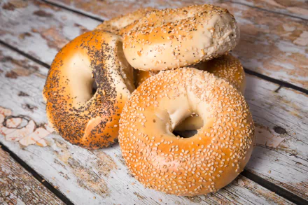 2K Quad HD PC desktop wallpaper: close-up of three bagels (sesame and poppy seed) on a rustic wooden surface, bread/food background.