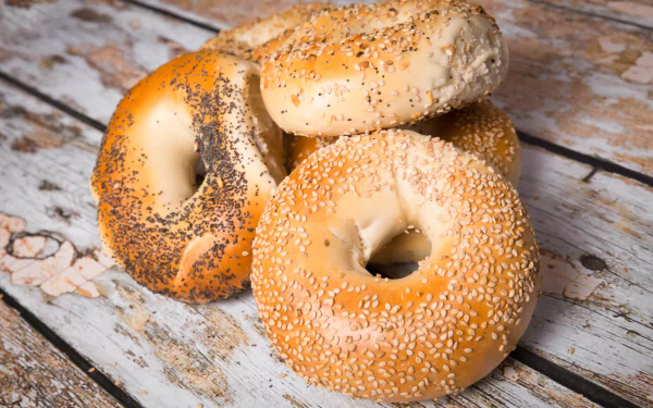 2K Quad HD PC desktop wallpaper: close-up of three bagels (sesame and poppy seed) on a rustic wooden surface, bread/food background.