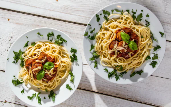 2K Quad HD still-life desktop wallpaper: two plates of spaghetti with tomato sauce, basil and parsley on a white wooden table — appetizing meal and food photography.