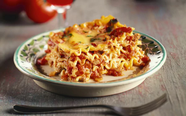 2K Quad HD PC desktop wallpaper: close-up meal of lasagna on a patterned plate, layered pasta, rich meat-tomato sauce and melted cheese with a fork nearby.