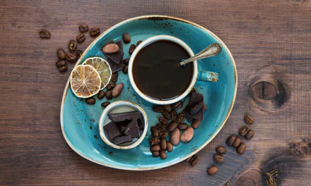 HD desktop wallpaper featuring a still life arrangement with a cup of coffee, coffee beans, and pieces of chocolate on a vibrant turquoise plate. The image exudes a cozy and inviting food and coffee theme.