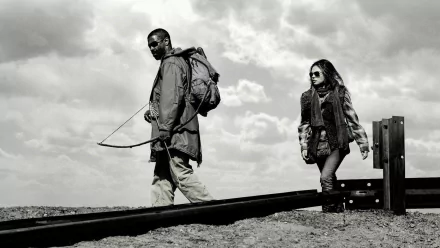 Black-and-white HD desktop wallpaper featuring Denzel Washington and Mila Kunis from the movie The Book of Eli, walking along a rail track under a cloudy sky.