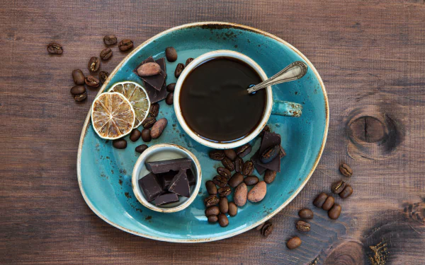 HD desktop wallpaper featuring a still life arrangement with a cup of coffee, coffee beans, and pieces of chocolate on a vibrant turquoise plate. The image exudes a cozy and inviting food and coffee theme.