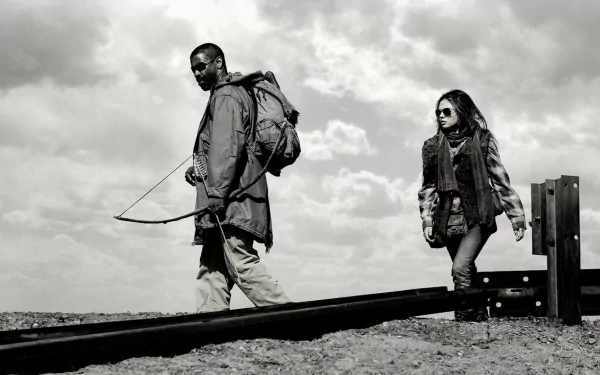 Black-and-white HD desktop wallpaper featuring Denzel Washington and Mila Kunis from the movie The Book of Eli, walking along a rail track under a cloudy sky.