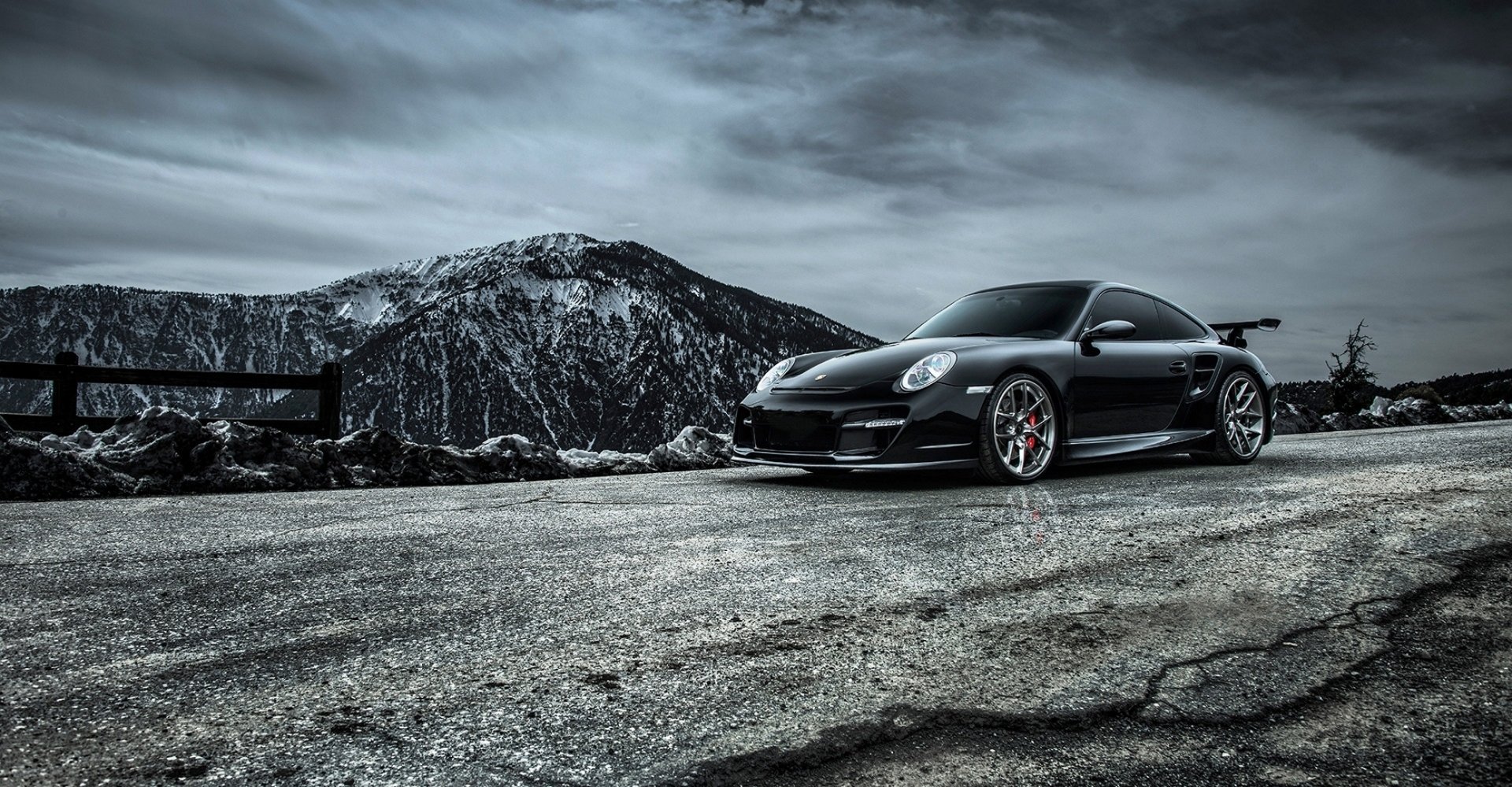 Black Porsche 911 Carrera parked on a rugged mountain road under a dramatic cloudy sky, captured as an HD desktop wallpaper and background.