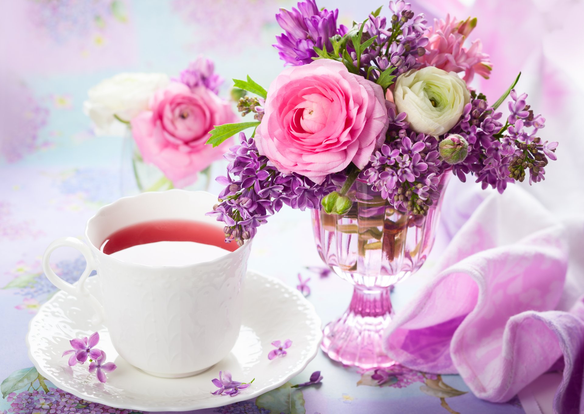 A 4K Ultra HD still life PC wallpaper featuring a vase of lilac, ranuncula, peony, and purple and pink flowers alongside a white cup of tea, set in a soft spring scene.
