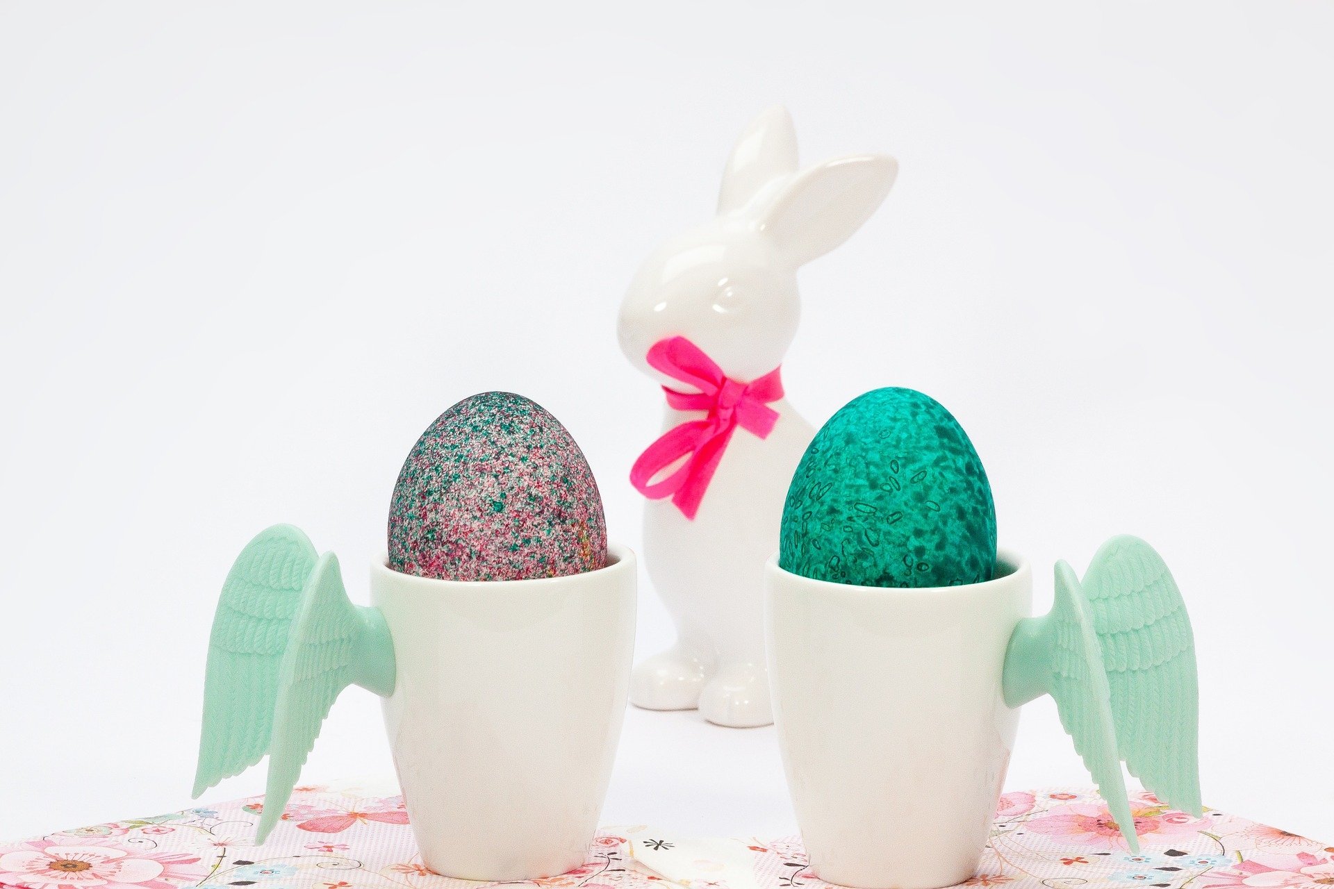 HD PC desktop wallpaper featuring two decorated Easter eggs in winged cups with a white bunny figurine tied with a pink ribbon, capturing the holiday spirit.