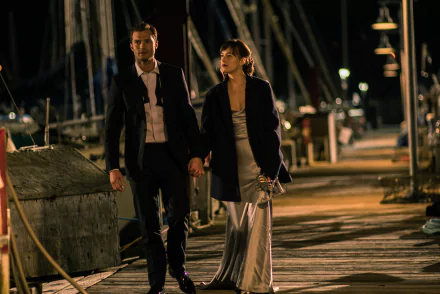 A scene from Fifty Shades Darker featuring Dakota Johnson and Jamie Dornan walking hand in hand on a dock at night. A HD desktop wallpaper and background.