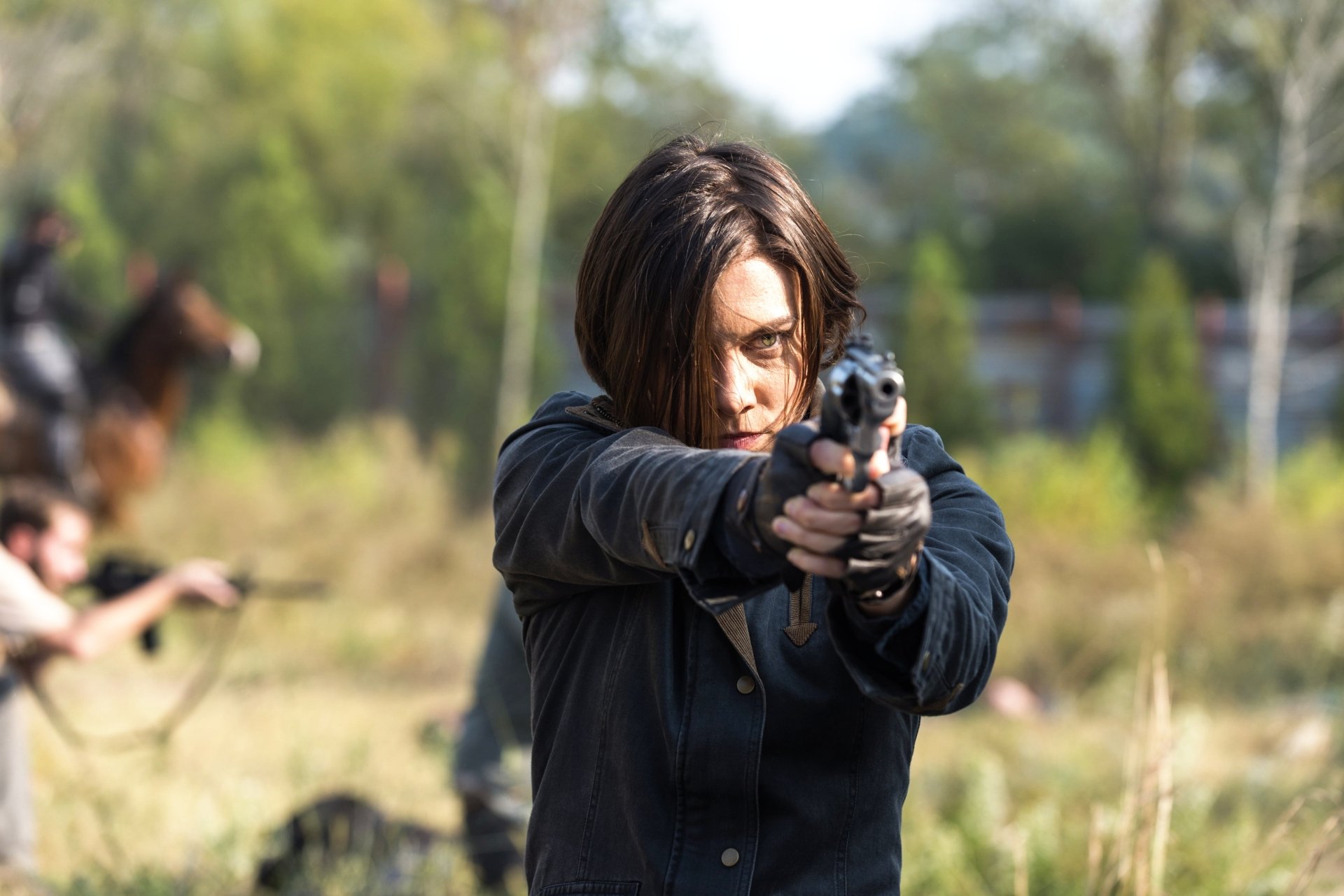 Maggie Greene, played by Lauren Cohan in The Walking Dead, aims a pistol in a tense outdoor scene, captured in a 4K Ultra HD TV show wallpaper.