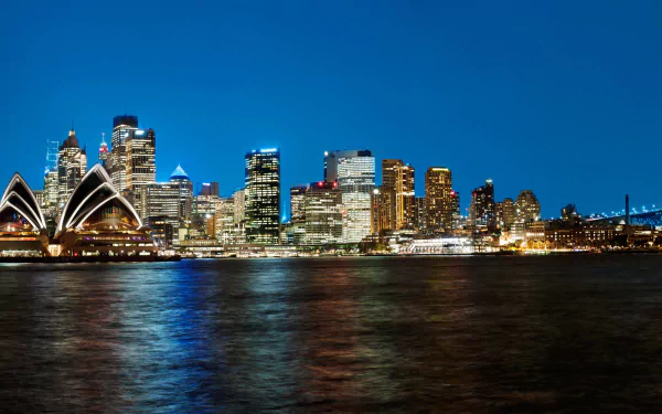 HD desktop wallpaper showcasing the Sydney Opera House and city skyscrapers illuminated at night, reflecting on the water in Australia.